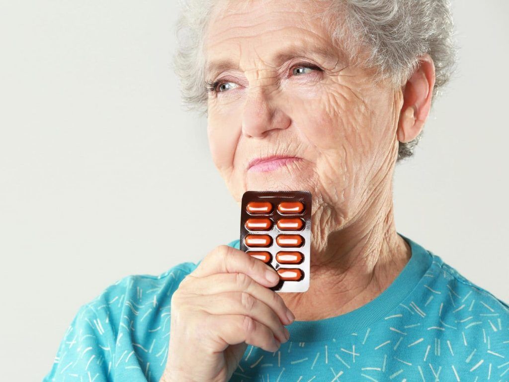 senhora idosa pensa na cura do alzheimer segurando uma cartela de comprimidos